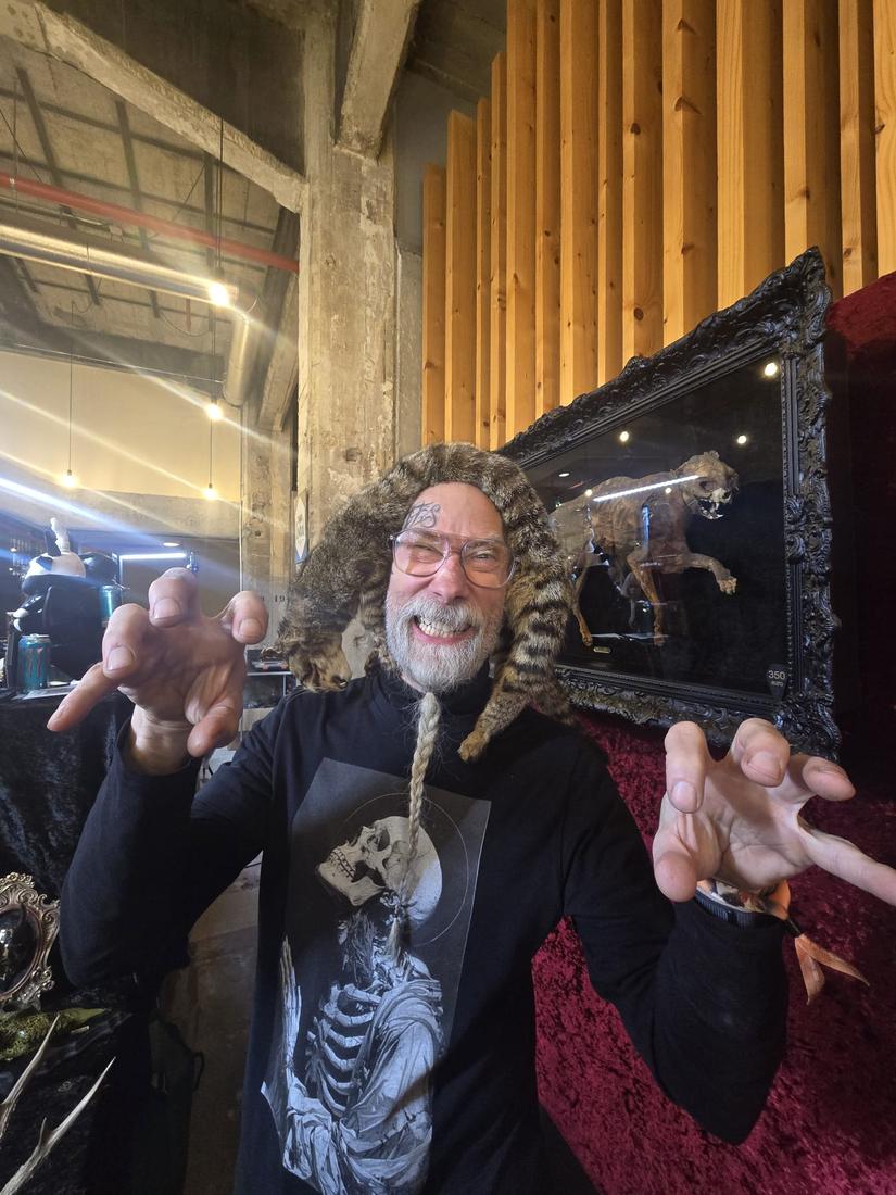 Flipke grinning with a cat pelt draped over his head, behind an ornate mirror.