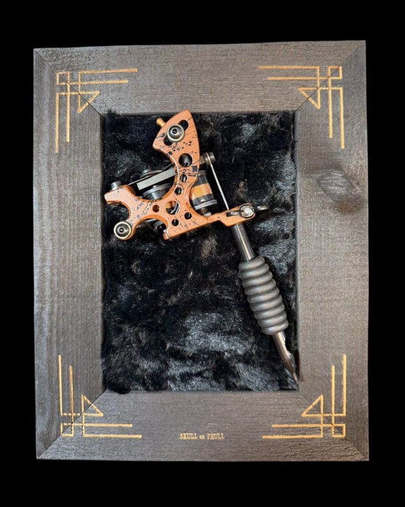 Orange tattoo machine on black fur in a grey art deco frame