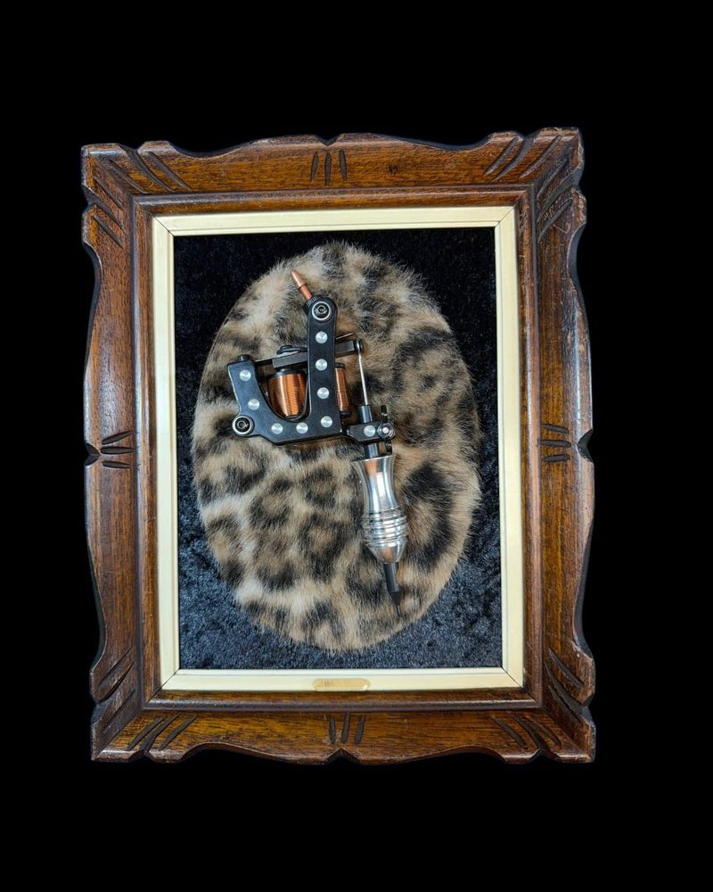 Tattoo machine mounted on leopard print fur in a carved wood frame